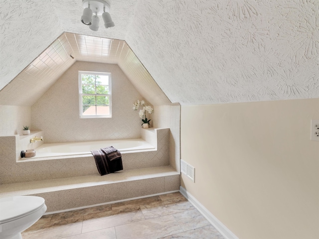 bathroom featuring a textured ceiling, vaulted ceiling, tiled tub, tile patterned flooring, and toilet