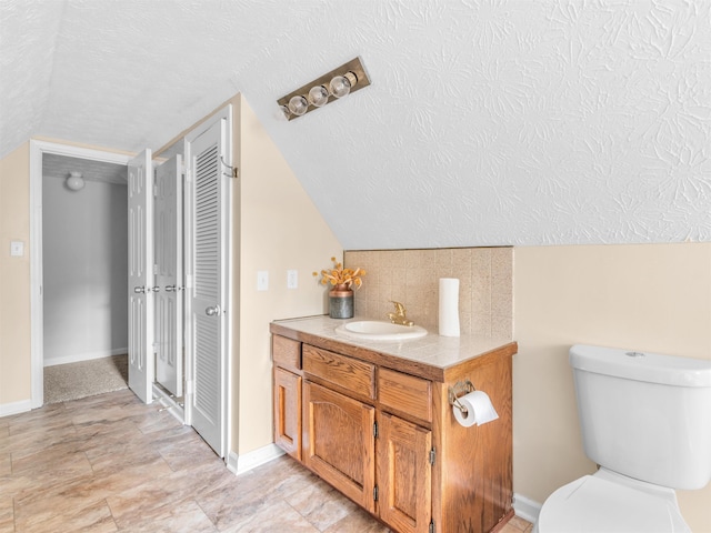 bathroom with vaulted ceiling, vanity, a textured ceiling, and toilet