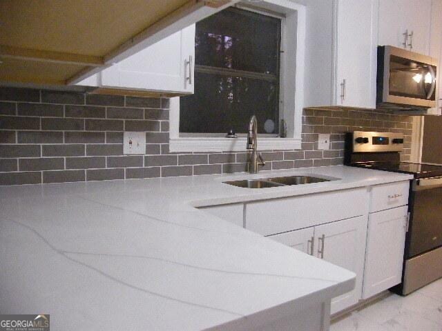 kitchen with white cabinets, stainless steel appliances, sink, and backsplash