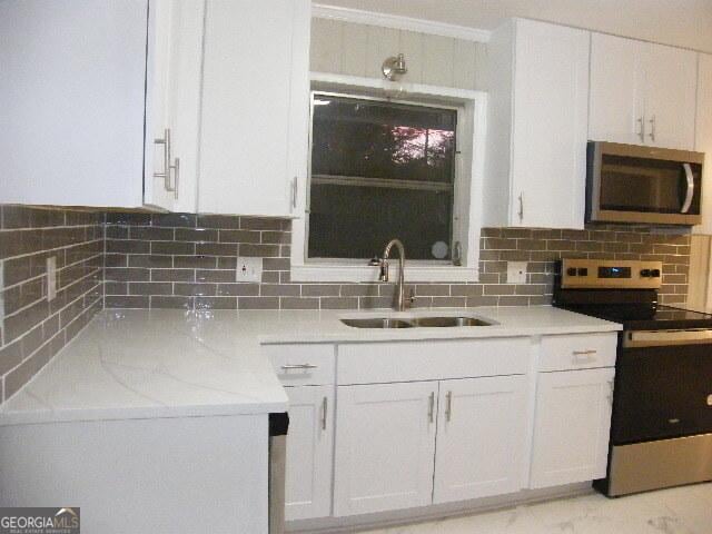 kitchen with sink, stainless steel appliances, tasteful backsplash, light stone counters, and white cabinets