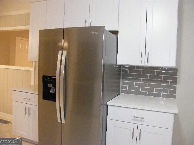 kitchen with stainless steel refrigerator with ice dispenser, white cabinets, and decorative backsplash