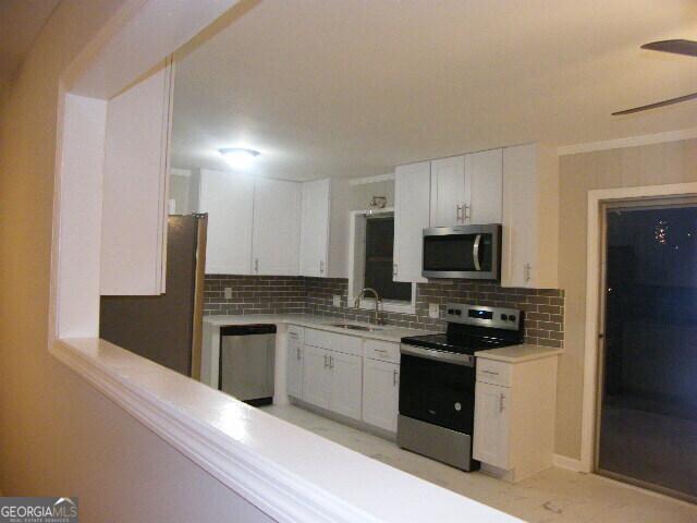 kitchen featuring appliances with stainless steel finishes, white cabinetry, sink, decorative backsplash, and ceiling fan