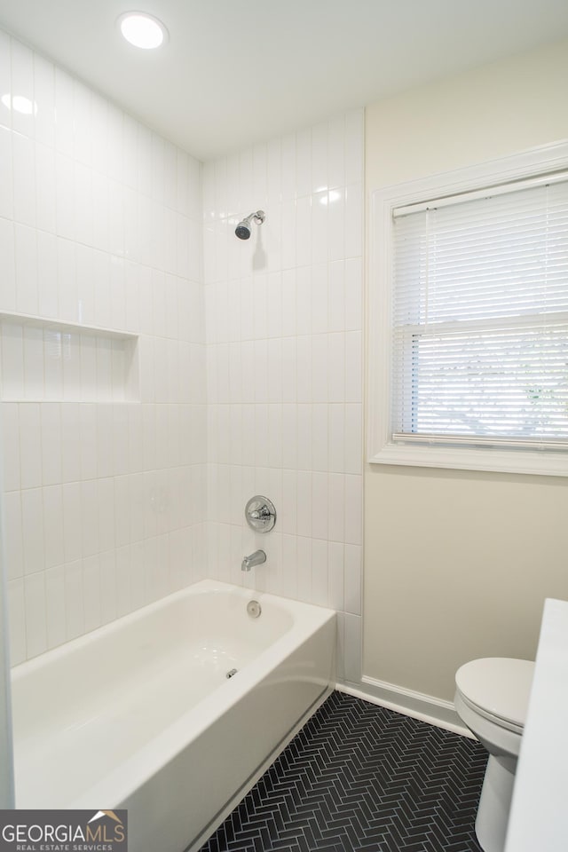 bathroom with tile patterned flooring, tiled shower / bath combo, and toilet