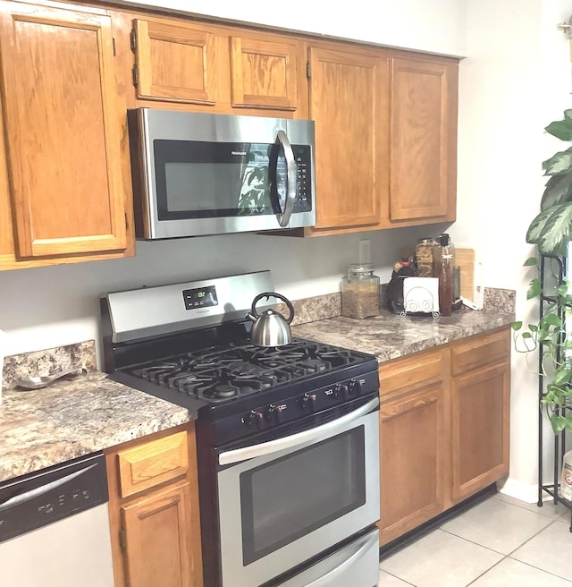 kitchen with light tile patterned floors, stainless steel appliances, and dark stone counters