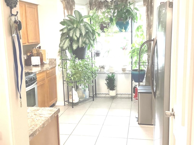 kitchen with stainless steel electric range oven, light tile patterned floors, light stone counters, and fridge