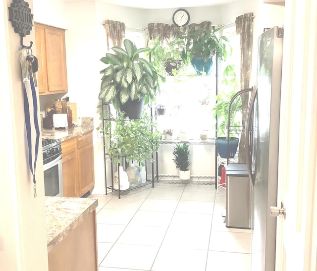 kitchen with stainless steel electric stove, light stone counters, light tile patterned floors, and fridge