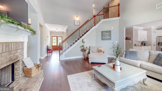 living room with crown molding, a towering ceiling, dark wood-type flooring, and a brick fireplace