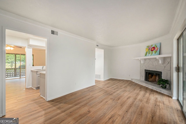 unfurnished living room featuring ornamental molding, a stone fireplace, and light wood-type flooring