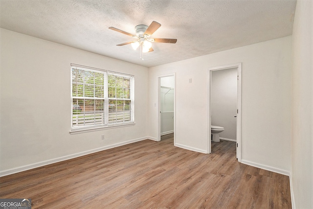 unfurnished bedroom featuring connected bathroom, a walk in closet, light hardwood / wood-style flooring, a closet, and ceiling fan