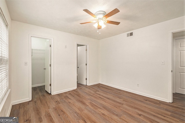 unfurnished bedroom with hardwood / wood-style flooring, ceiling fan, a textured ceiling, a walk in closet, and a closet