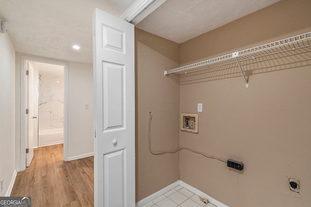 washroom featuring electric dryer hookup, washer hookup, light hardwood / wood-style floors, and a textured ceiling