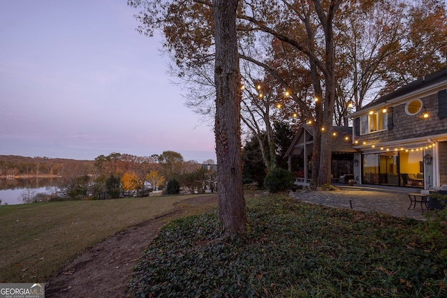 yard at dusk with a water view and a patio