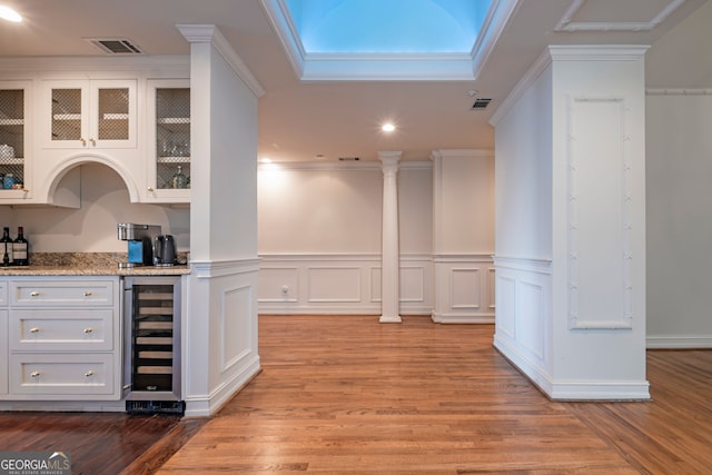 bar featuring wine cooler, light stone counters, crown molding, light hardwood / wood-style floors, and white cabinetry