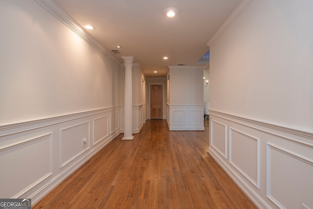 corridor featuring light wood-type flooring, ornate columns, and ornamental molding