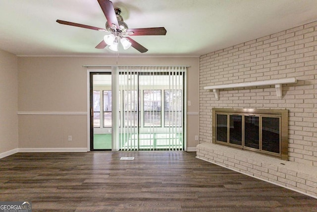 unfurnished living room with ceiling fan, ornamental molding, dark wood-type flooring, and a brick fireplace