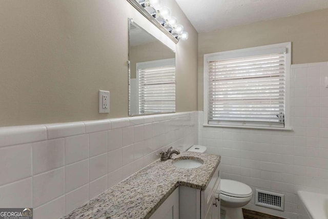 bathroom featuring vanity, a bathtub, toilet, and tile walls