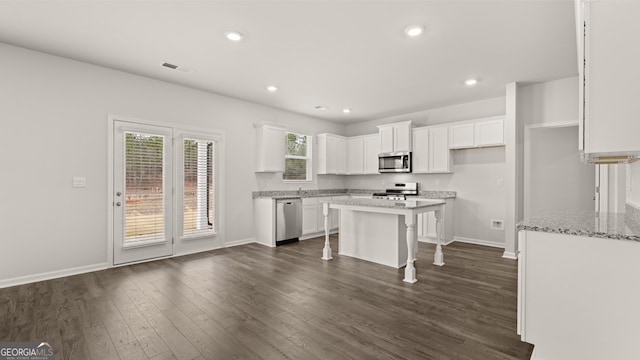 kitchen featuring dark wood-type flooring, stainless steel appliances, a kitchen island, a breakfast bar area, and white cabinets