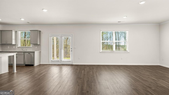 unfurnished living room with a sink, baseboards, crown molding, and dark wood finished floors