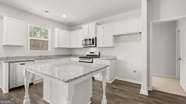 kitchen with white cabinets, sink, appliances with stainless steel finishes, a kitchen island, and light stone counters