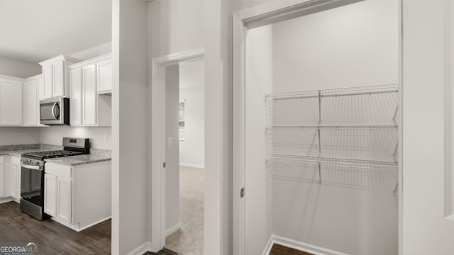 interior space with white cabinetry, dark hardwood / wood-style flooring, light stone countertops, and appliances with stainless steel finishes