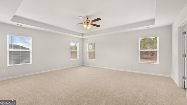 carpeted empty room with ceiling fan, a raised ceiling, and a wealth of natural light