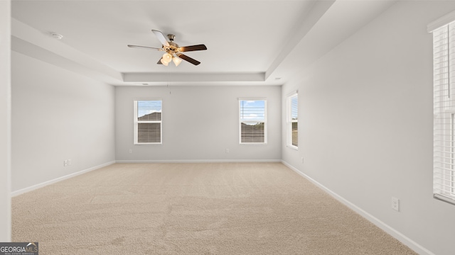 empty room with a raised ceiling, ceiling fan, and light colored carpet