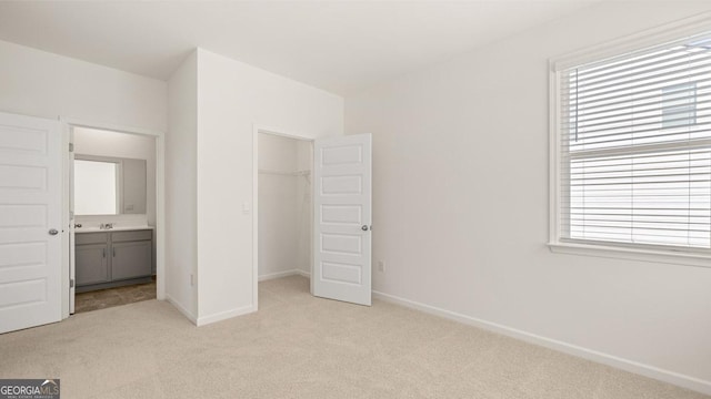 unfurnished bedroom featuring a closet, baseboards, a walk in closet, and light carpet