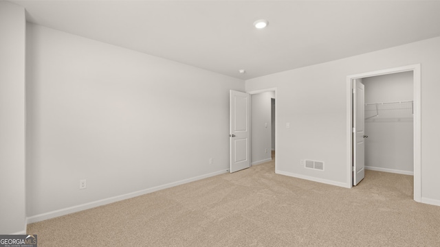 unfurnished bedroom featuring a walk in closet, light carpet, and a closet