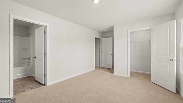 unfurnished bedroom featuring connected bathroom, light carpet, and a spacious closet