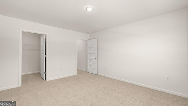unfurnished bedroom featuring a spacious closet, baseboards, a closet, and light carpet