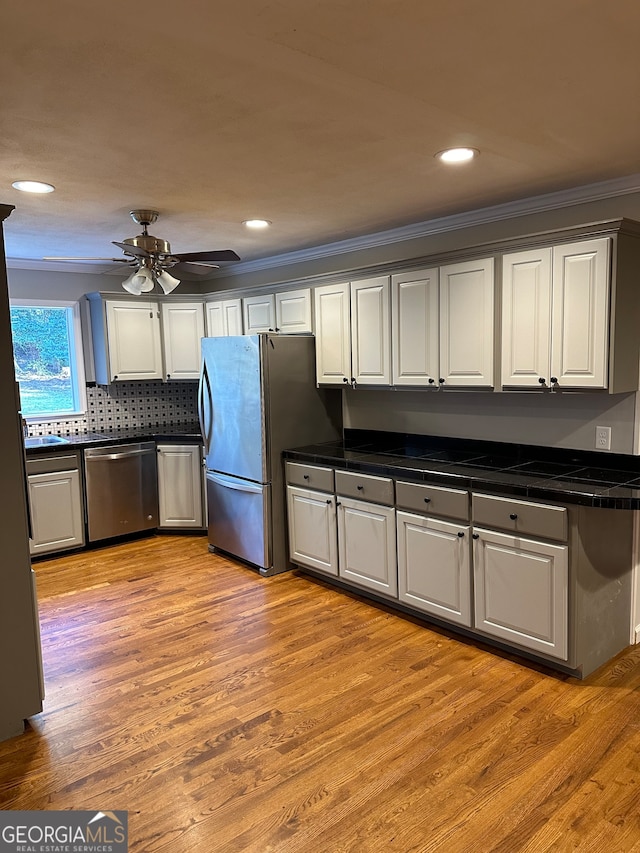 kitchen featuring crown molding, light hardwood / wood-style flooring, ceiling fan, appliances with stainless steel finishes, and tasteful backsplash