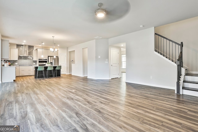 unfurnished living room featuring hardwood / wood-style floors and ceiling fan with notable chandelier