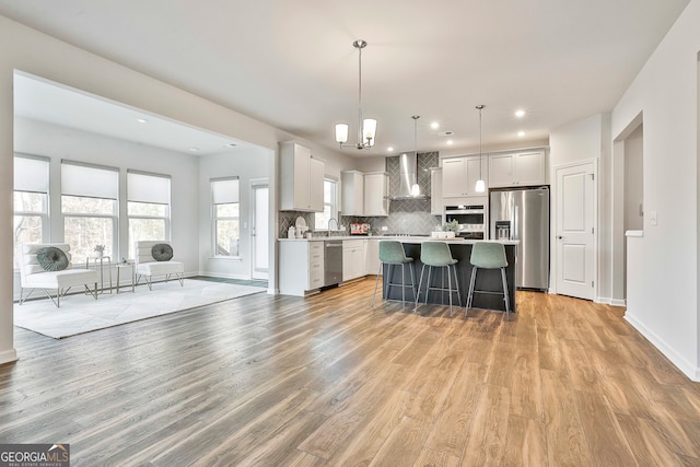 kitchen featuring a kitchen island, wall chimney range hood, stainless steel appliances, and light hardwood / wood-style flooring