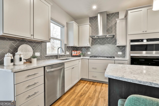 kitchen with sink, wall chimney exhaust hood, backsplash, light hardwood / wood-style floors, and appliances with stainless steel finishes