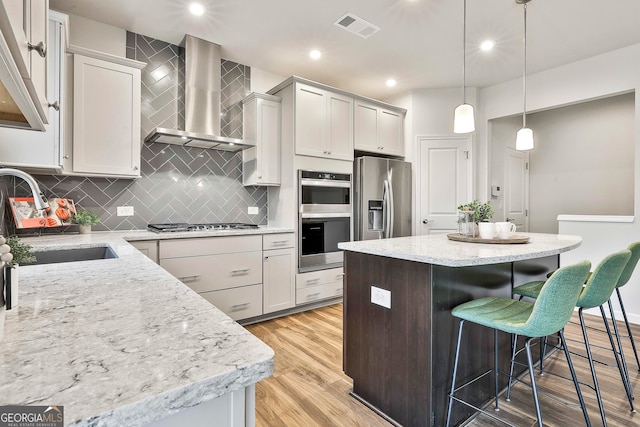 kitchen with sink, wall chimney exhaust hood, light hardwood / wood-style floors, a kitchen island, and stainless steel appliances