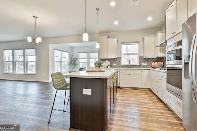 kitchen featuring white cabinets, a kitchen bar, hanging light fixtures, and light hardwood / wood-style flooring