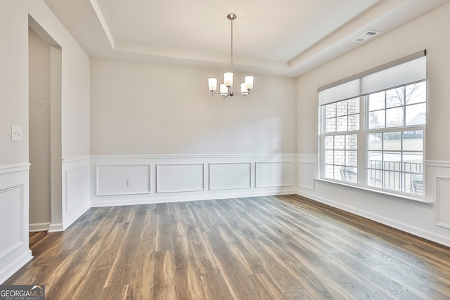 empty room with dark hardwood / wood-style flooring, a tray ceiling, and an inviting chandelier