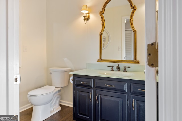 half bathroom with baseboards, toilet, wood finished floors, and vanity