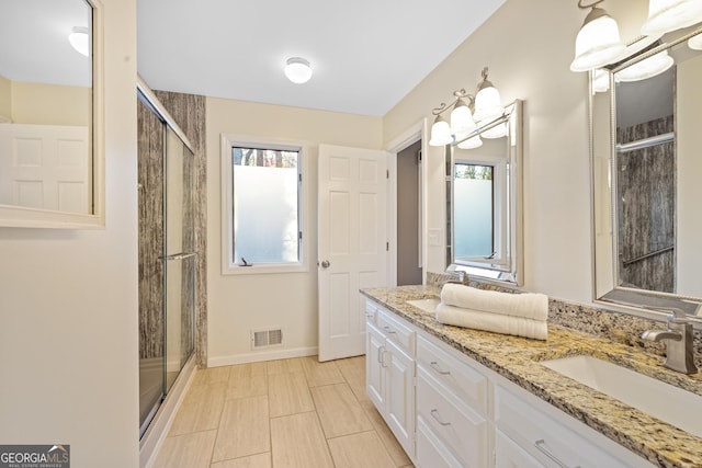 full bathroom with visible vents, a sink, a shower stall, double vanity, and baseboards