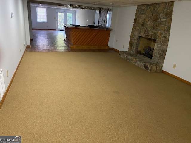 unfurnished living room featuring wood-type flooring, a stone fireplace, and french doors