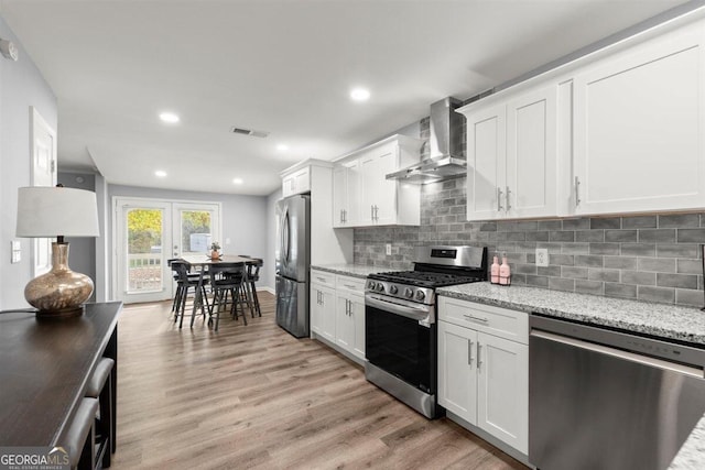 kitchen featuring white cabinetry, wall chimney exhaust hood, stainless steel appliances, light stone counters, and light hardwood / wood-style flooring