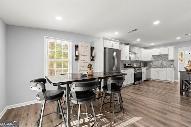 kitchen featuring wall chimney exhaust hood, stainless steel appliances, decorative backsplash, white cabinets, and light wood-type flooring