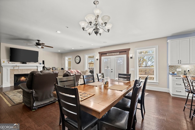 dining space with a tile fireplace, french doors, ceiling fan with notable chandelier, and dark hardwood / wood-style floors