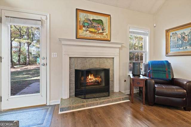 living area with a tile fireplace, hardwood / wood-style floors, vaulted ceiling, and a wealth of natural light