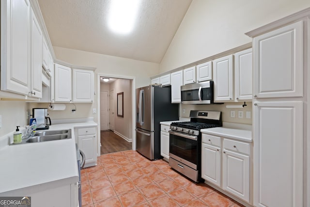 kitchen with appliances with stainless steel finishes, a textured ceiling, white cabinetry, and lofted ceiling