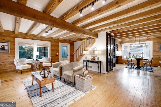 living room featuring beamed ceiling, wood walls, light wood-type flooring, and a wealth of natural light