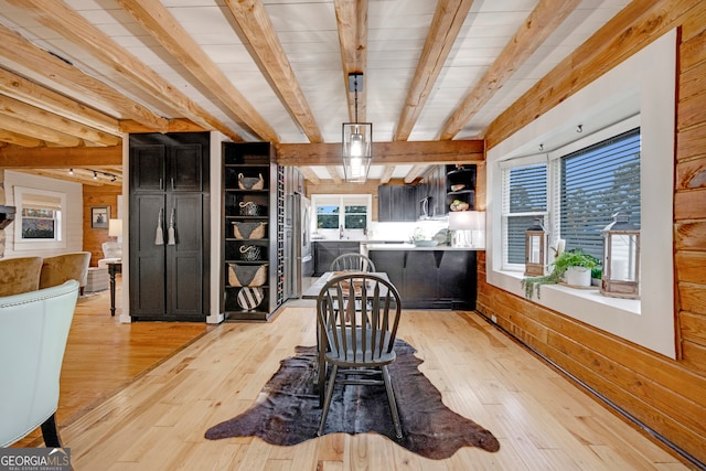 dining room featuring wooden walls, beamed ceiling, and light hardwood / wood-style floors