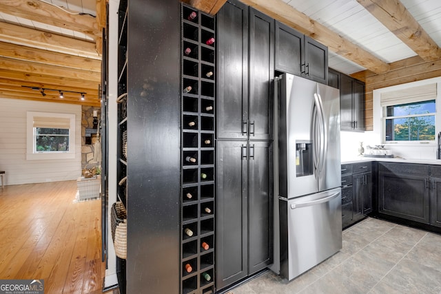 kitchen with beam ceiling, stainless steel fridge with ice dispenser, a healthy amount of sunlight, and light wood-type flooring