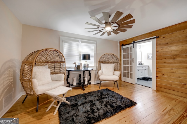 living area with hardwood / wood-style floors, ceiling fan, a barn door, and wooden walls