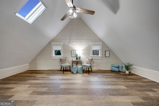 sitting room with vaulted ceiling with skylight, ceiling fan, wood walls, and hardwood / wood-style flooring